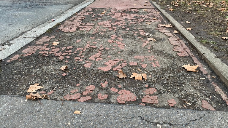 Radweg mit abgenutzten Belag und Rissen.
