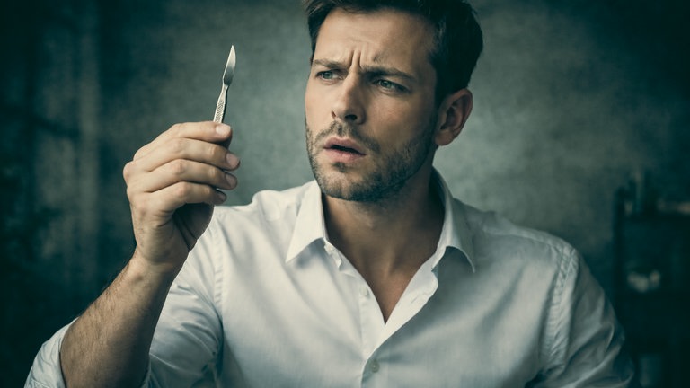 Person in Hemd hält ein kleines Skalpell in der Hand