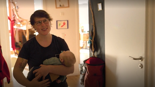 Eine Frau mit Baby auf dem Arm öffnet ihre Wohnungstür