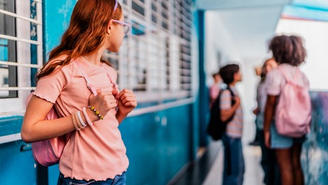 Ein Mädchen schaut traurig zu Mitschülern, die sich unterhalten. Die Schule geht wieder los. Das kann ein Auslöser für Einsamkeit sein. Bild: iStockFG Trade Latin