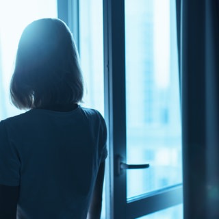 Eine Person alleine im Dunkeln, Lichter einer Stadt im Hintergrund. 