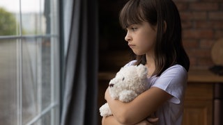 Nahaufnahme kleines Mädchen umarmt sein Kuscheltier und blickt aus dem Fenster 
