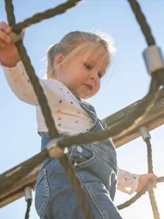 Ein kleines Mädchen klettert auf einem Spielplatz.