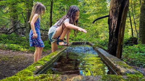 Zwei Kinder spielen an einem Wasserspielplatz im Wald