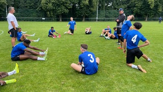 Fußballer dehnen sich auf einem Platz in Karlsruhe.