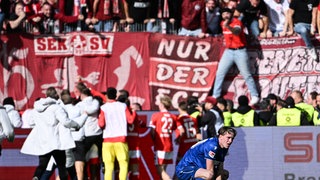 Im Vordergrund geht David Herold vom KSC in die Knie, im Hintergrund feiern die FCK-Spieler mit ihren Fans