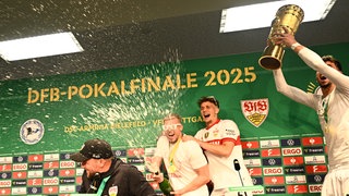 Stuttgarts Trainer Sebastian Hoeneß (vorn) wird auf der Pressekonferenz nach dem Pokalsieg von seinen Spielern mit Bier begossen