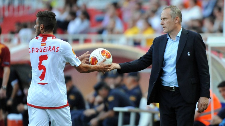 SC-Freiburg-Trainer Christian Streich (rechts im dunkelblauen Sakko mit hellblauem Hemd) übergibt den Ball an Diogo Jose Rosario Gomes Figueiras (links im weißen Trikot) vom FC Sevilla