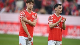 Die Mainzer William Bøving und Paul Nebel stehen mit hängenden Köpfen vor der Fankurve. Sie ärgern sich über den vergebenen Sieg gegen de VfB Stuttgart.