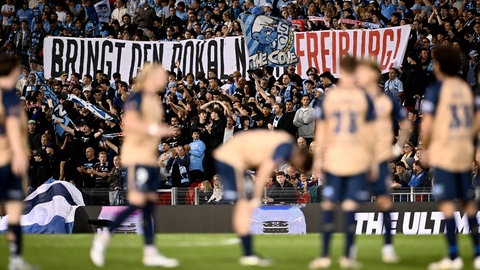 Anhänger von Sydney FC halten ein Banner zur Unterstützung des SC Freiburg nach oben