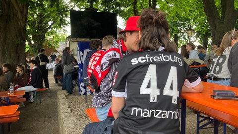 Fans in Trikots des SC Freiburg warten im Kastaniengarten in Freiburg auf den Anpfiff