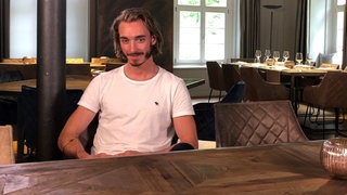 Der ehemalige Radprofi Dominik Nerz sitzt mit einem weißen T-Shirt in seinem neuen Restaurant und starrt ins Leere.