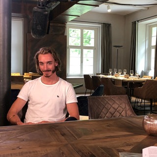 Der ehemalige Radprofi Dominik Nerz sitzt mit einem weißen T-Shirt in seinem neuen Restaurant und starrt ins Leere.