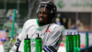 Der Schwarze Eishockeyspieler Jalen Smereck lehnt an der Bande der Ersatzbank der Bietigheim Steelers und schaut auf die vor ihm aufgereihten grünen Getränkeflaschen.