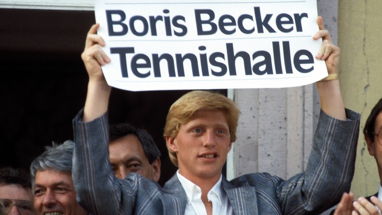 Boris Becker hält auf dem Rathausbalkon ein Schild in die Höhe auf dem steht "Boris Becker-Tennishalle"