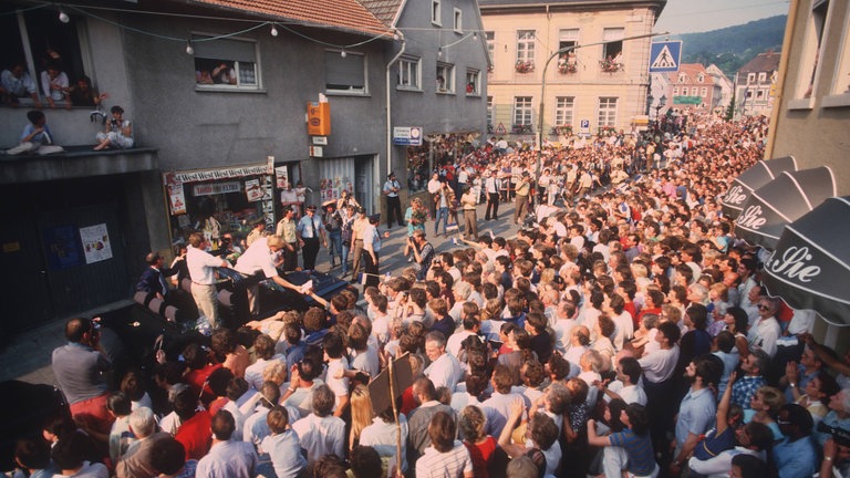 Boris Becker steht in einem fahrenden Auto und jubelt von dort den Fans auf den Straßen in Leimen zu