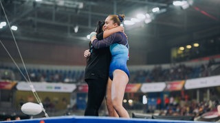 Meolie Jauch (TS NeckarGym Nürtingen) freut sich mit ihrer Trainerin über Gold am Stufenbarren