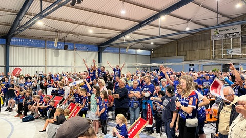Hunderte Fans in blauen Trikots feiern in einer Halle. Der HBW Balingen-Weilstetten ist in die erste Handball-Bundesliga aufgestiegen und Meister geworden.