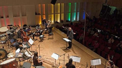 Musiker sitzen auf Podium, Mann dirigiert sie
