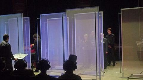 Menschen mit Kopfhörern und Musiker hinter angeleuchteten Glaswänden