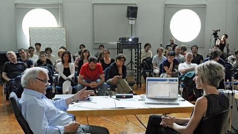 Älterer Herr und jüngere Frau diskutieren vor vielen Zuhörern