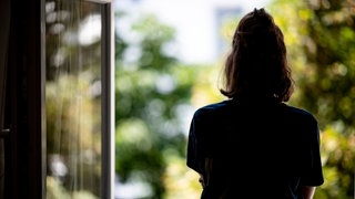 Eine Frau steht in ihrer Wohnung an einem Fenster