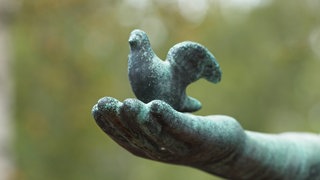 Steinskulptur eines Vogels auf einer Hand auf einem Friedhof