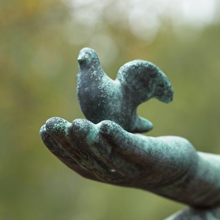 Steinskulptur eines Vogels auf einer Hand auf einem Friedhof