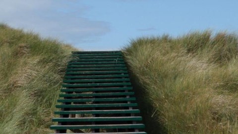 Hügel mit Gras bewachsen und Treppen, dahinter der Himmel