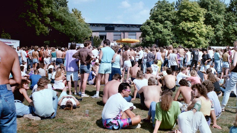 Viele Menschen sitzen 1989 im Park der Villa Berg in Stuttgart, hören gemeinsam Radio und warten auf das Finale der SDR3 Hitparade TOP 1000 X