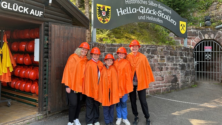 Der perfekte Tag mit SWR1 im Nordschwarzwald. Unsere Gewinnergruppe steht mit orangenem Regenschutz und Helmen vor dem Silber-Bergwerk "Hella-Glück-Stollen".