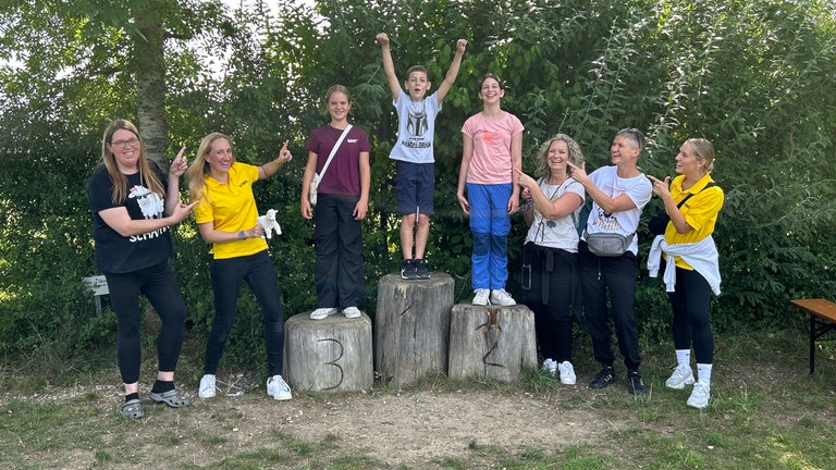 Der perfekte Tag mit SWR1 im Nordschwarzwald. Eine Gruppe von Menschen feiert die Siegerehrung von drei Kindern, die auf Podesten aus Baumstümpfen stehen.