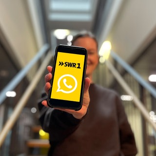 SWR1 Moderatorin Cora Klausnitzer hält ein Smartphone. Darauf zu sehen sind die Logos von SWR1 und Whatsapp.