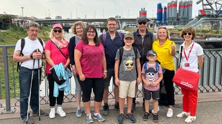 Die Gewinner des perfekten Tages stehen auf einer Brücke am Mannheimer Hafen. Verena freut sich mit ihren Schwiegereltern Rudi und Helga, ihrer Schwester Martina, ihrem Mann Philipp, ihren Söhnen Julian und Hannes, ihrem Schwager Thomas, SWR1-Moderatorin Janet Pollok und Stadtführerin Elli Strittmatter-Halfer