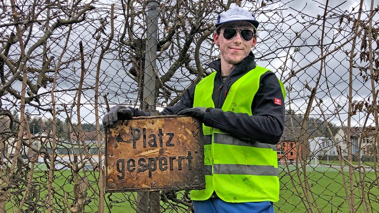 Mit Sonnenbrille, Mütze, gelber Weste und Handschuhen hat Jan in der Donau ein Metallschild aus der Donau gefischt.