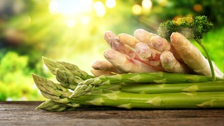 Grüner und weißer Spargel liegt auf einem Holzbrett.