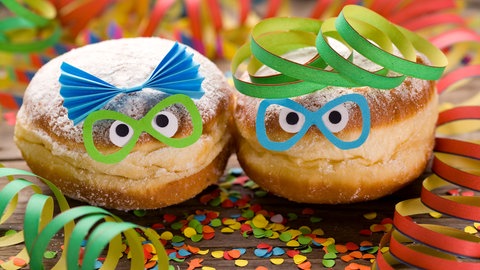 SWR1 Pfännle meets Fasnacht - wir feiern Fasnet, Fastnacht, Fasching und Karneval kulinarisch! Küchenkäpsele und Rezepte für Fasnachtsküchle, Nonnenfürzle und mehr.  Das Bild zeigt einen Berliner  Krapfen im Faschingskostüm: Maske, Konfetti und Luftschlangen