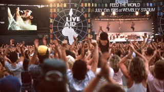 Vor 40 Jahren: Die Fans jubeln während des Live Aid Auftritts von Queen-Sänger Freddie Mercury.  | 40 Jahre Live Aid: Das größte Rockkonzert der Geschichte