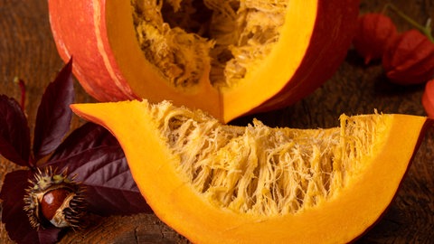 Ein aufgeschnittener Kürbis liegt auf einer Holzplatte, daneben eine Rosskastanie. 