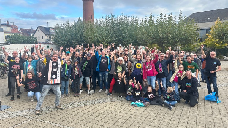 Gruppenfotos: Viele Menschen tragen Band-Shirts und stehen in einer Gruppe zusammen.