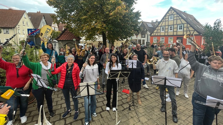 Menschen stehen mit Instrumenten auf einem Platz und freuen sich.