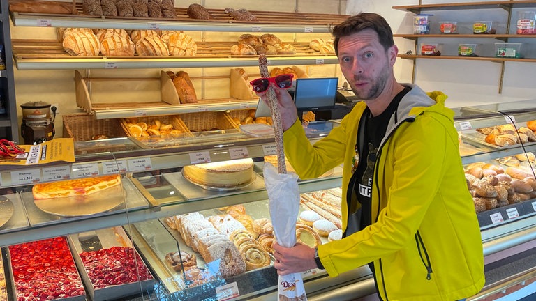 Moderator Corvin Tondera-Klein hält ein Backteilchen mit Sonnenbrille in der Hand.