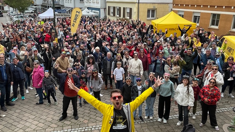 Große Gruppe steht mit Sonnenbrillen beisammen, vorne steht Moderator Corvin Tondera-Klein und breitet die Arme aus. 