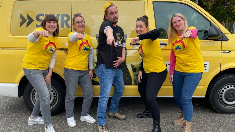 Ingo Lege steht in der Mitte von jeweils zwei Frauen in gelben T-Shirts. Sie machen eine Boyband nach.