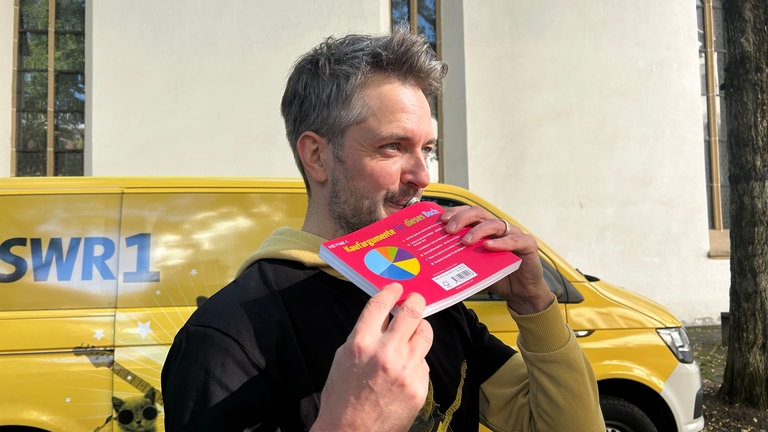 Bene hat sein Instrument vergessen, aber immerhin ans Mundstück gedacht: Mitten im Bücherflohmarkt auf dem Kirchplatz in Blaubeuren spielt er sich warm für das HITmach-Duell.