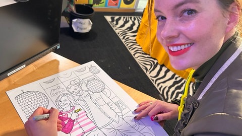 Moderatorin Cora Klausnitzer malt ein Ausmalbild aus mit dem Motov Stefanie Anhalt und Corvin Tondera-Klein.