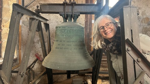 Hilke aus Sternenfeld posiert neben einer großen Kirchenglocke