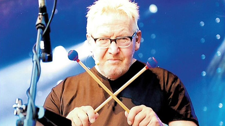 Matthias Holtmann mit gekreuzten Drumsticks am Schlagzeug. Er schaut entschlossen in die Kamera.