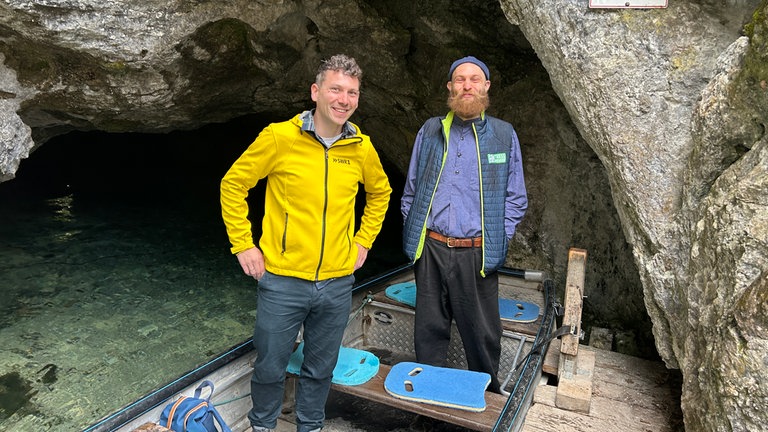 SWR1 Moderator Julian Hammerstein steht auf einem Boot vor der Wimsener Höhle mit Bootsführer Valentin.