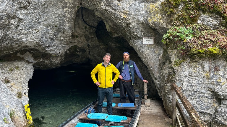 SWR1 Moderator Julian Hammerstein steht auf einem Boot vor der Wimsener Höhle mit Bootsführer Valentin.